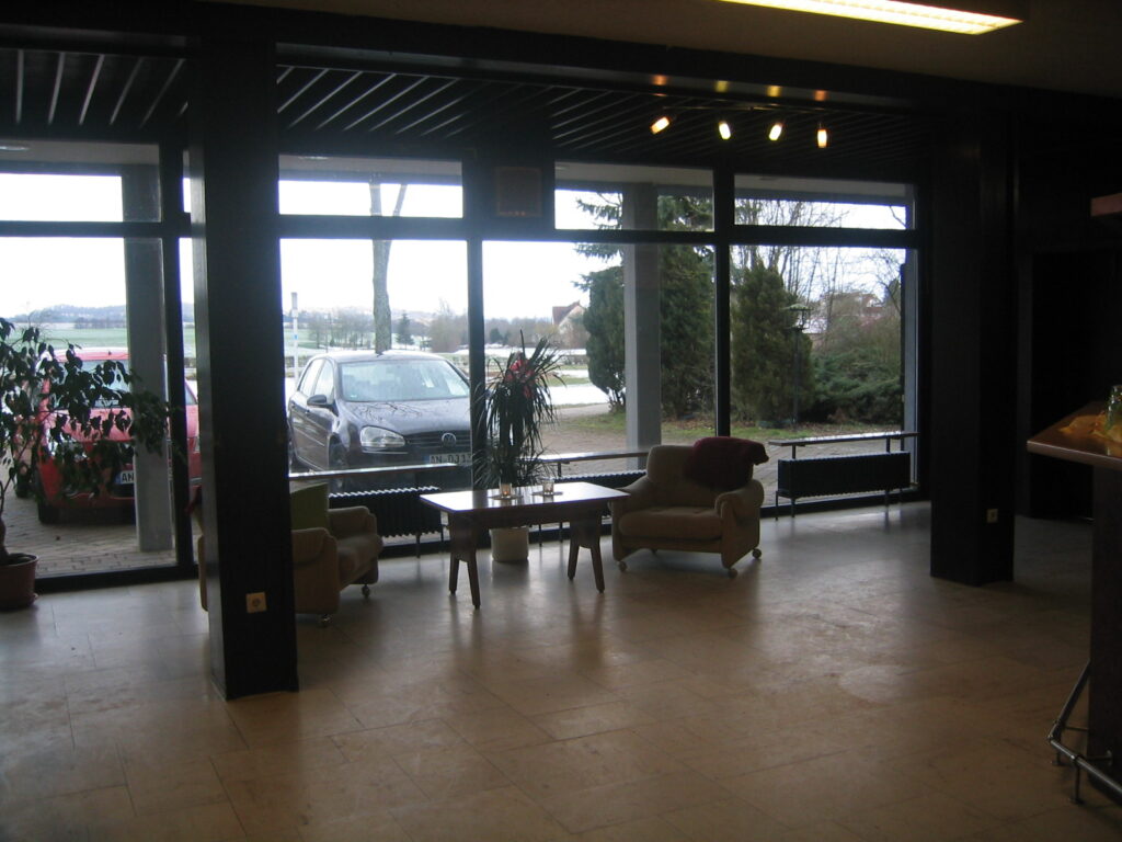 Heller Empfangsbereich mit Sitzgruppe und Blick auf geparkte Autos. Neues Zuhause.