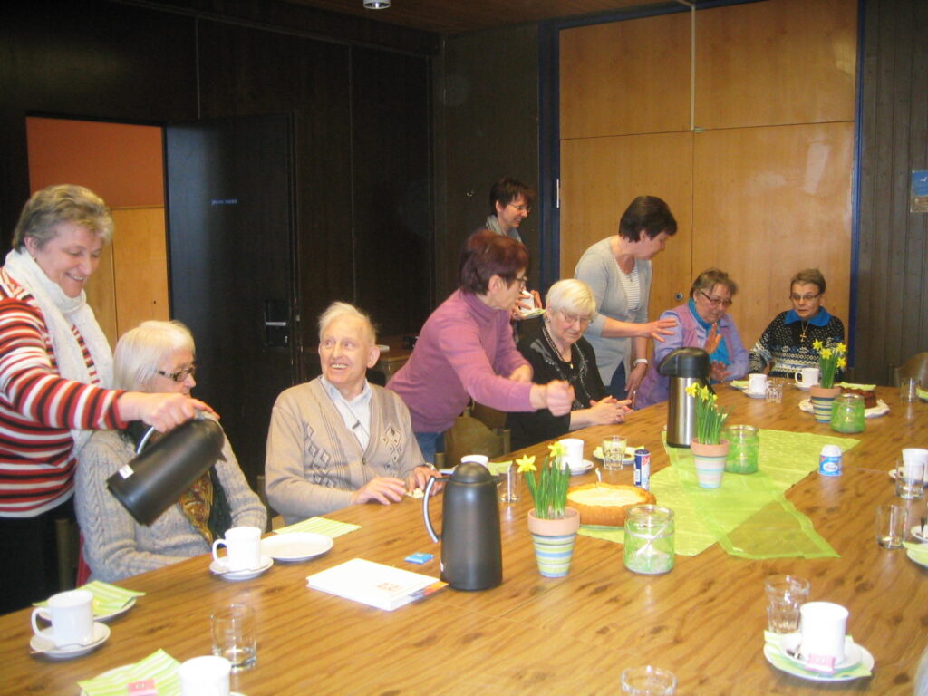 Betreuungsgruppe: Senioren sitzen am Tisch, Kaffee wird eingeschenkt.