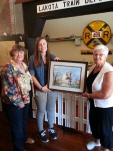 Drei Frauen im Lakota Train Depot halten ein gerahmtes Bild. Heimat, Erinnerung an seine Herkunft.