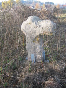 Steinkreuz oder Sühnekreuz auf einer Wiese, gesichert mit Metallplatten.