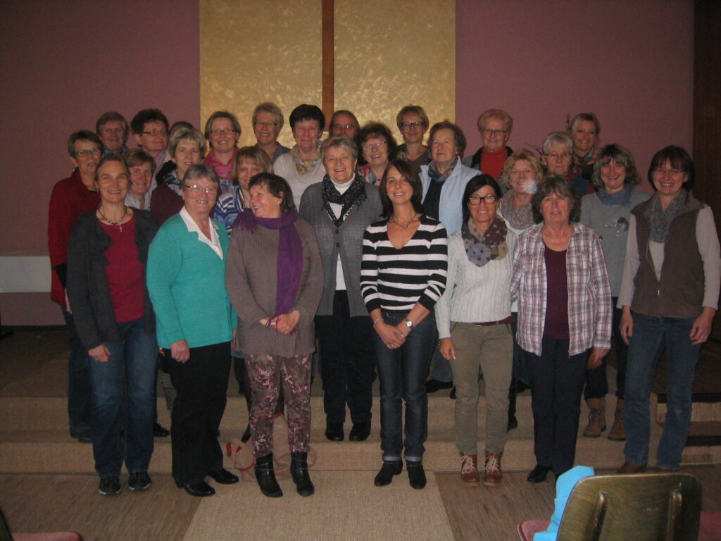 Gruppenfoto unserer Mitarbeiterinnen vor einem goldenen Kreuz.