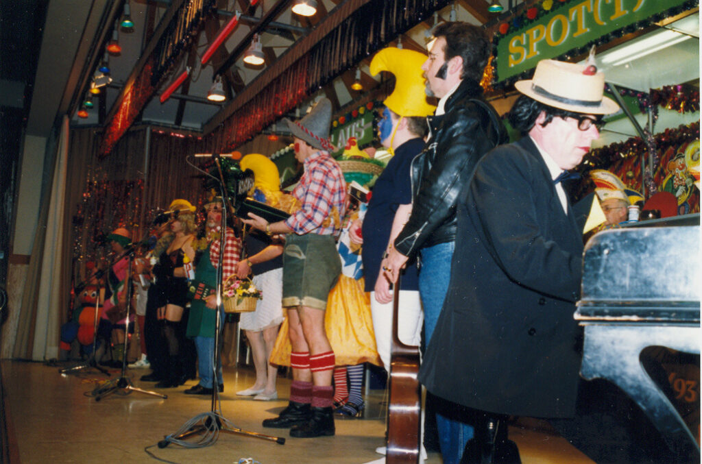 Karneval celebration: People in costumes on stage, one playing piano.