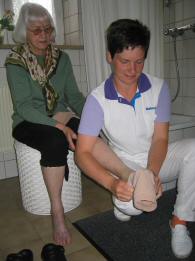 Frau hilft älterer Dame beim Anziehen von Kompressionsstrümpfen.