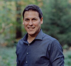 Headshot of a smiling man in a blue shirt, Vorstand.
