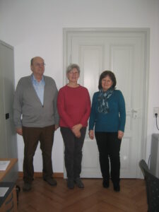 Three staff members stand in an office. "Unsere Mitarbeitenden" blog content.