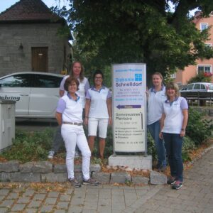 Group of Diakonie Schnelldorf staff standing next to their sign. Diakonie Schnelldorf provides ambulatory care.